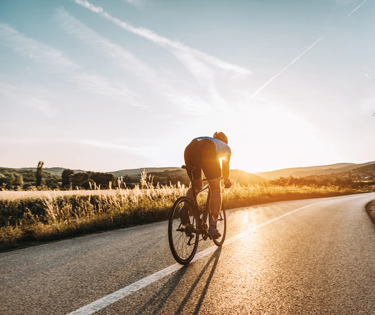 Fahrradfahrer faehrt auf einer leeren Straße bei Sonnenuntergang