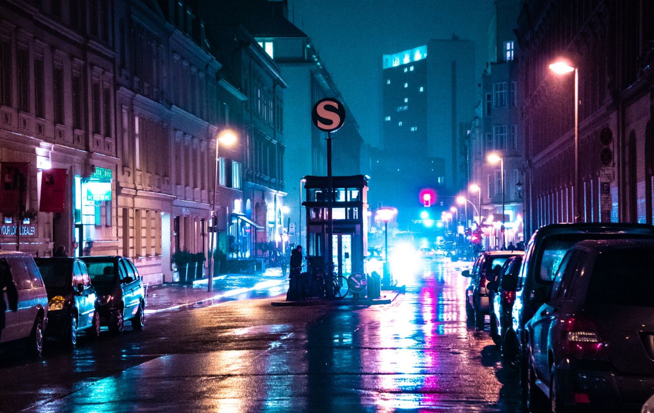 Eine beleuchtete Stadtstraße bei Nacht, mit bunten Lichtern und geparkten Autos