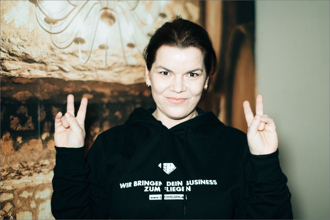 Sabrina Bergmann zeigt Peace-Zeichen, trägt schwarzen Hoodie mit Werbeaufdruck