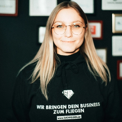 Nele Ohmstede steht lächelnd in einem Büro mit Logos an der Wand.